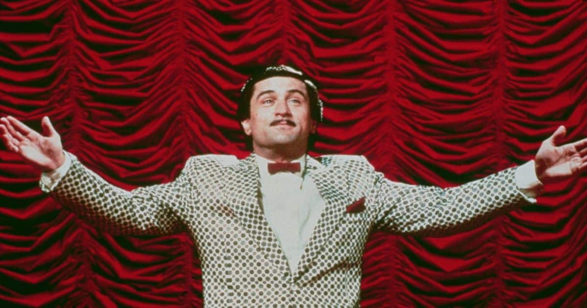 Robert De Niro abre los brazos frente a una cortina roja en El rey de la comedia