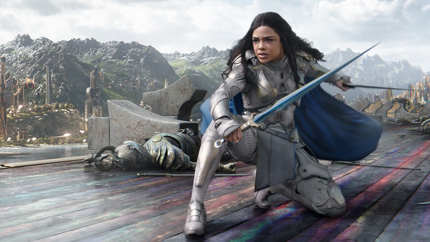 Mujer con espada y armadura se arrodilla con espada defensivamente frente a ella.