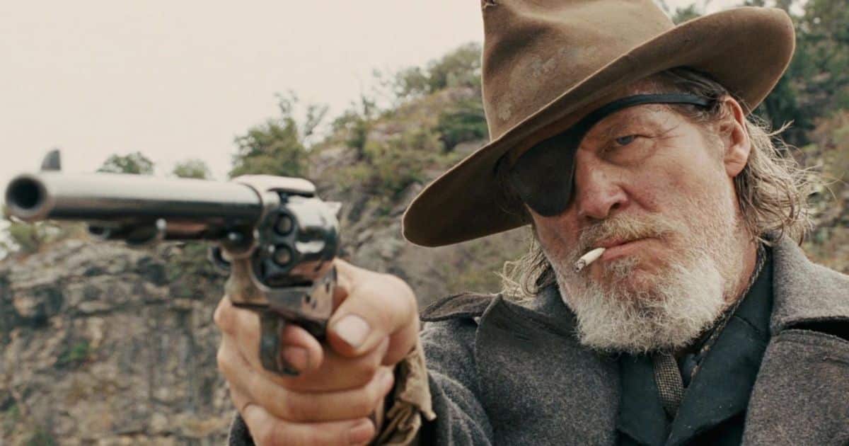 El mariscal estadounidense Rooster Cogburn (Jeff Bridges) luciendo un parche en el ojo, un sombrero de vaquero y un cigarrillo, empuñando un revólver en True Grit.
