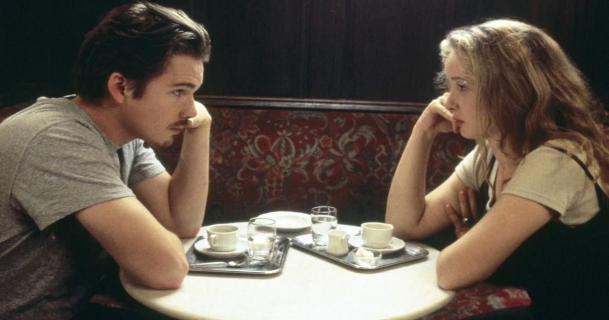 Julie Delpy y Ethan Hawke sentados y citando en una mesa en Before Sunrise.